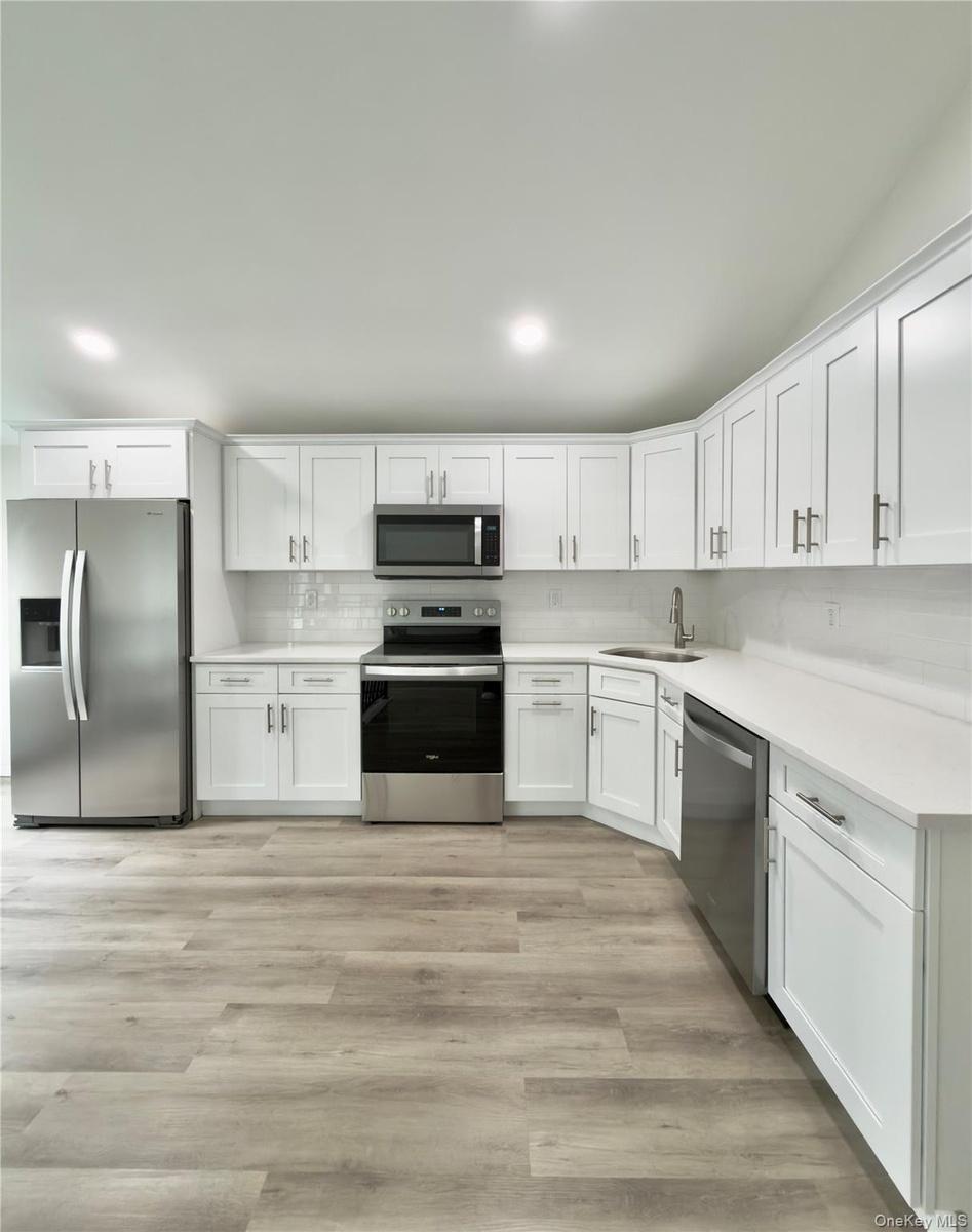 White cabinetry with brushed nickel hardware, stainless steel appliances, light-toned countertops, subway tile backsplash.