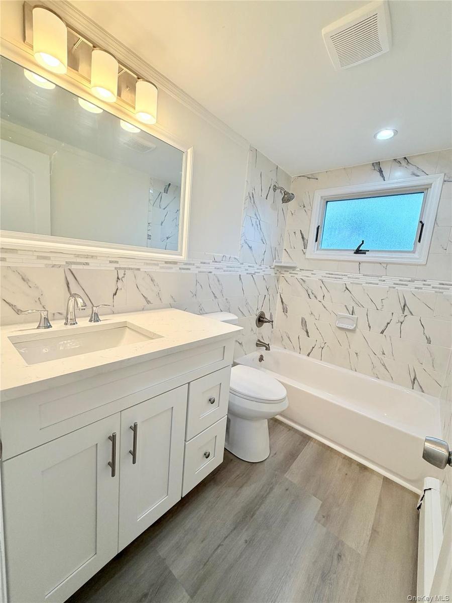 Bathroom featuring a single vanity with stone-finish countertop and  built-in bathtub.