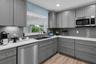 Updated kitchen features gray custom cabinetry with soft-close drawers, quartz countertops and sleek gray tile backsplash.