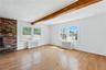 Unfurnished living room featuring light wood-style flooring, radiator, beam ceiling, and a brick fireplace