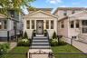 Paved entryway leading to a staircase with black railings, a black security door, and a manicured front yard with mature plantings and a wrought iron 