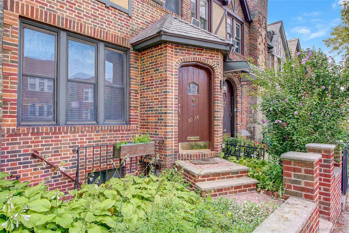 Brick facade with arched entry door, sheltered by an overhang, featuring stone steps and wrought iron railings