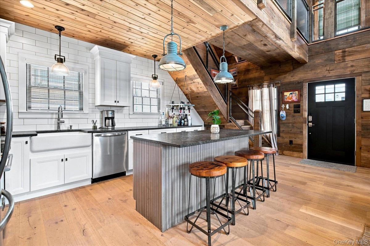 Hardwood flooring throughout, white shaker cabinetry, subway tile backsplash, stainless steel appliances, and a wood-paneled ceiling