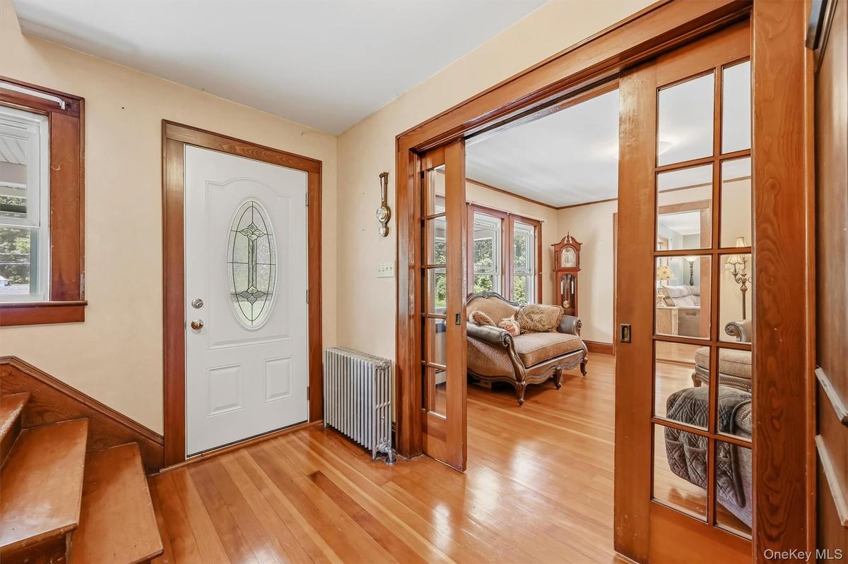 Front entry featuring hardwood floors, natural woodwork, and glass-paneled pocket doors leading into the living room.