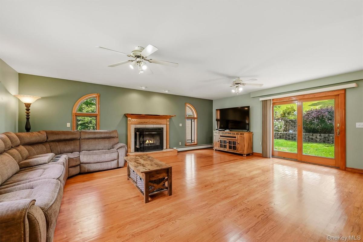 Spacious family room featuring hardwood floors, a fireplace, arched windows, and sliding glass doors leading to the backyard.