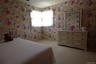 Wallpapered walls featuring a floral pattern, window with white lace curtains, and light-toned carpeting