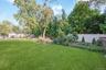 Expansive lawn area with surrounding mature trees, perimeter fencing, and cultivated garden beds