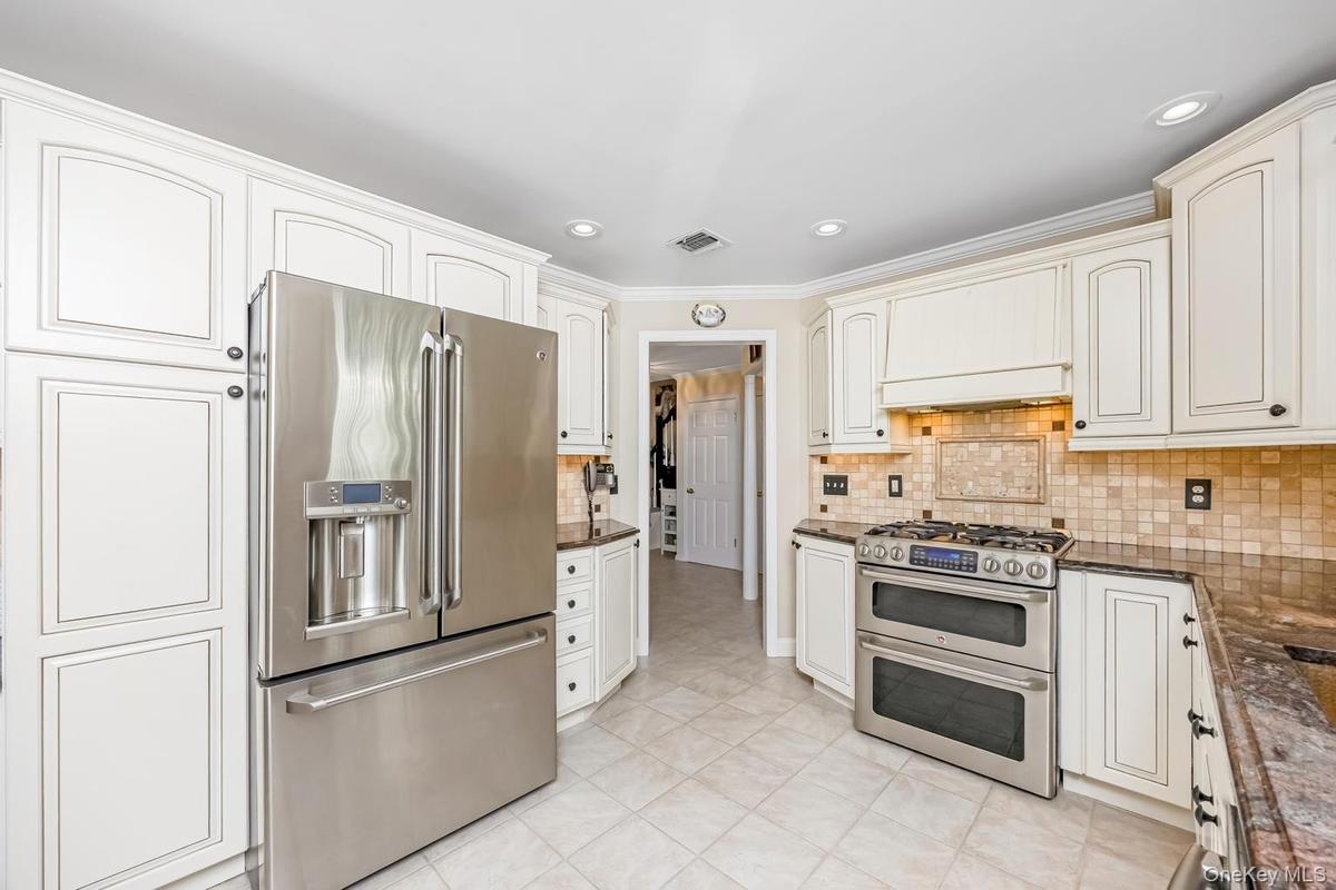 White shaker-style cabinetry, stainless steel French door refrigerator, stainless steel double oven range, mosaic tile backsplash, and light-toned til