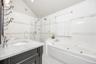 White tiled bathroom featuring a single vanity with stone countertop, glass-enclosed shower, built-in soaking tub, and black and white mosaic flooring