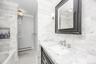 White marble tile walls, black framed mirror, white vanity sink, chrome faucet, and black and white patterned floor tile