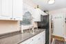 White cabinetry, a stainless steel sink, a countertop with a speckled finish, and a white paneled door with an arched glass insert