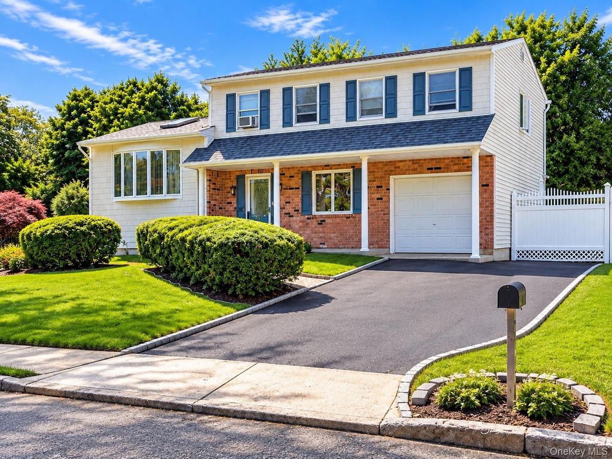Two-story exterior with brick and siding facade, covered entry, attached garage, paved driveway, and manicured landscaping