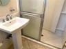 Pedestal sink with brushed metal faucet, framed shower enclosure with frosted glass, and tiled flooring