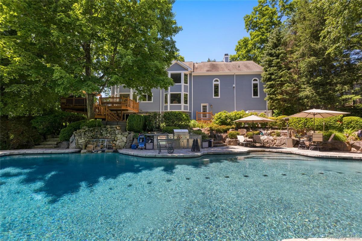 Rear view of house, deck, pool, patio and outdoor kitchen on a summer day.