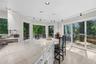View from inside the gleeaming white kitchen with walls of windows and sliding glass doors to the wrap-around deck with another outside kitchen area.