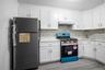 Kitchen featuring appliances with stainless steel finishes, white cabinetry, under cabinet range hood, light wood finished floors, and light stone cou