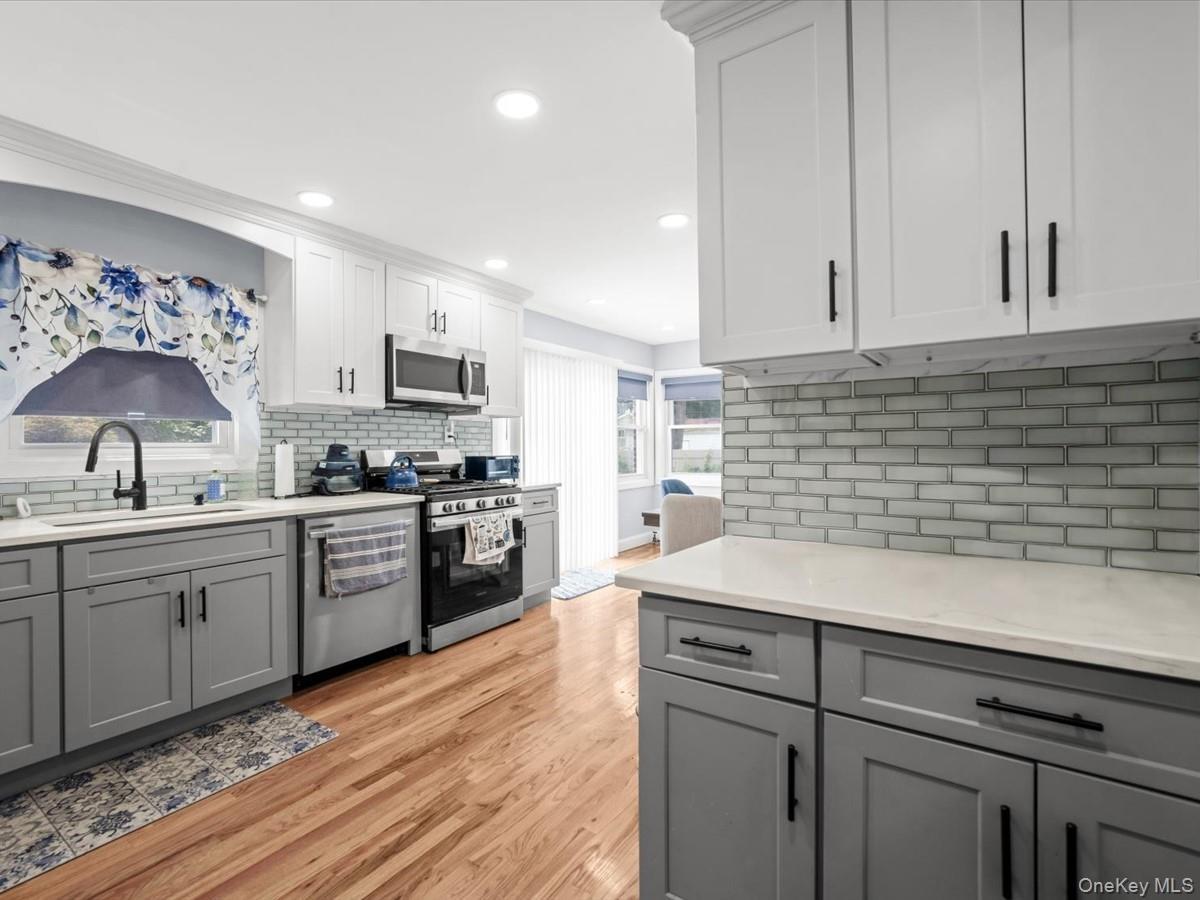 Two-tone cabinetry with white upper and gray lower cabinets, light-toned countertops, subway tile backsplash, stainless steel appliances, and wood-fin