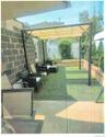 Outdoor covered patio with a retractable awning, concrete paver flooring, artificial turf, and a low brick retaining wall