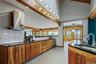 Vaulted ceiling with exposed wood beams, stainless steel range hood, natural wood cabinetry, black countertops, and a white subway tile backsplash