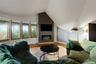 Recessed electric fireplace set in a dark-toned accent wall, light wood-finish flooring, and multiple large windows with natural wood frames