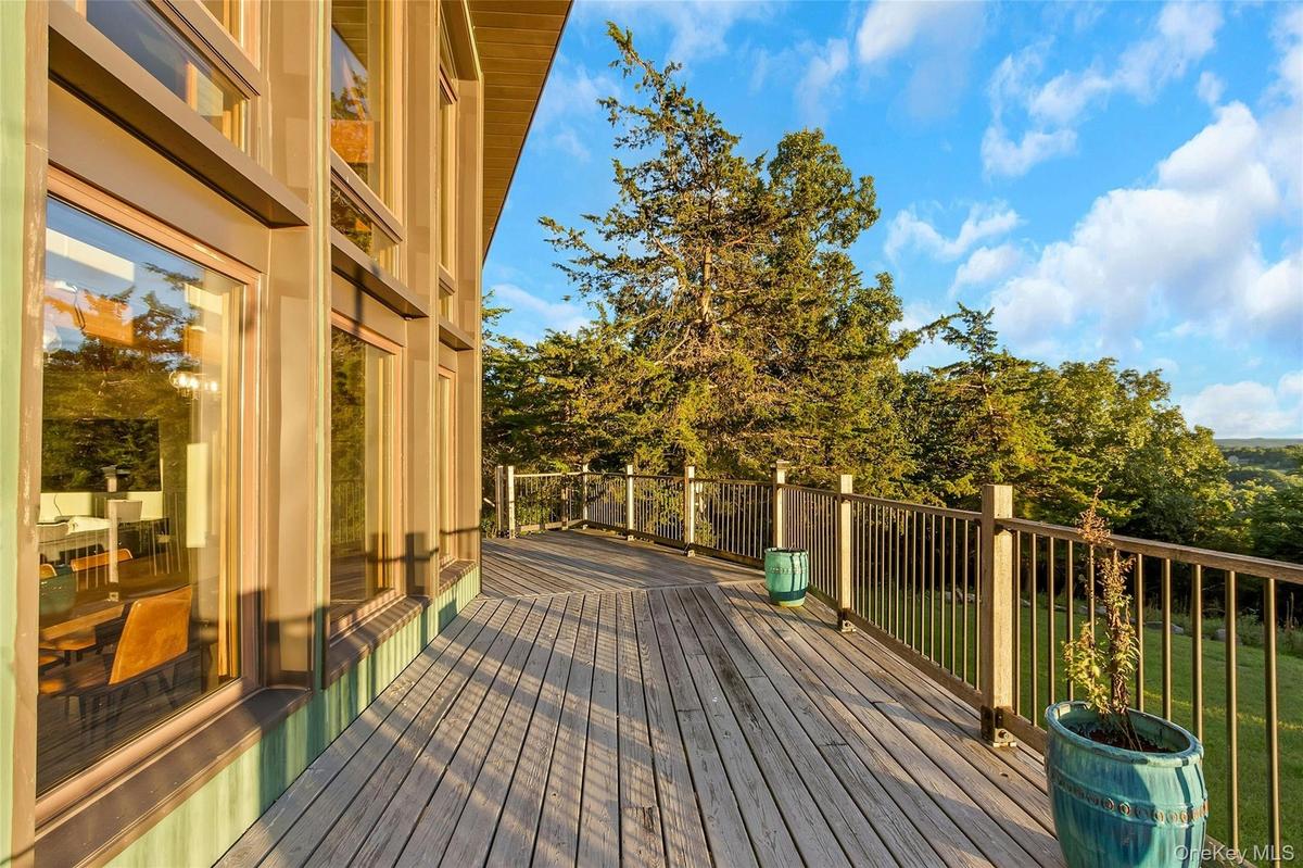 Expansive outdoor deck with wood plank flooring and metal railings, complemented by large vertical windows with wood frames