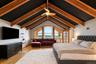 Vaulted ceiling with exposed wood beams, arched windows, light wood-finish flooring, and a ceiling fan