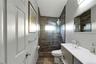 Bathroom featuring a walk-in shower with wood-finish tile surround, clear glass enclosure, and stone flooring