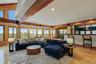 Expansive living space featuring exposed wood beams, wood-finish flooring, a full-height window wall, recessed lighting, and a built-in bar with count