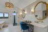 Freestanding soaking tub with gold accent, glass-enclosed shower with tiled accent wall, dual wall-mounted sinks, and ornate gold-framed mirrors