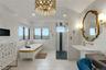 Freestanding soaking tub, walk-in shower with glass enclosure, single vanity with wall-mounted faucet, and a decorative overhead light fixture