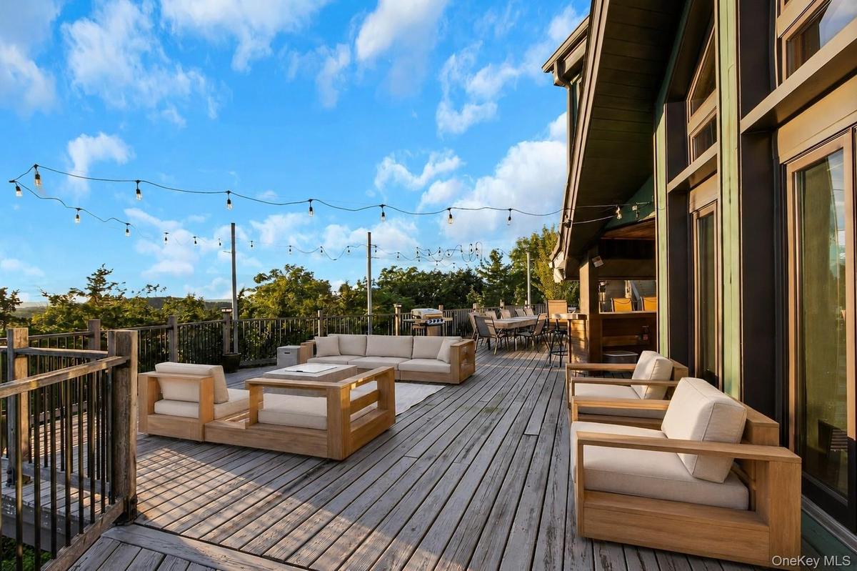 Expansive wood deck with string lighting, multiple seating areas, and a built-in outdoor kitchen