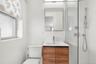 Tiled bathroom with a wood-finish vanity, integrated sink, mirrored medicine cabinet, and glass-enclosed shower