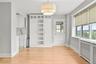 White built-in cabinetry with glass paneling, a contemporary tiered ceiling light fixture, and windows equipped with roller shades