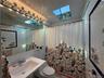 Bathroom featuring a skylight, white tile walls, a vanity with an integrated sink, and a large wall-mounted mirror with task lighting