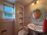 Bright, updated bathroom featuring ceramic tile walls, a pedestal sink with chrome fixtures, a round decorative mirror, and built-in wall shelving
