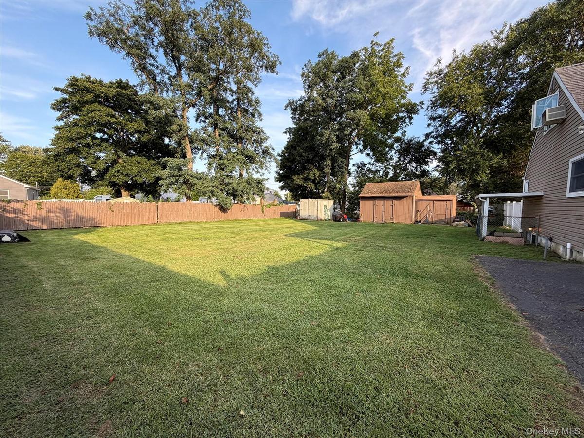 oversized rear yard with mature trees, a wood privacy fence, and two storage sheds