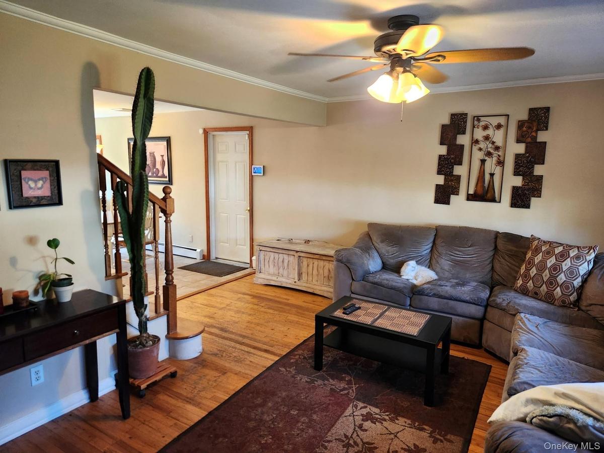 Hardwood flooring, painted walls, crown molding, ceiling fan with integrated lighting, and a staircase with wood railings
