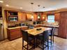 Wood-finish cabinetry with crown molding, stainless steel appliances, stone countertops, tiled backsplash, and recessed lighting