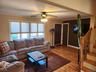 Hardwood flooring throughout, large window with cellular shades, ceiling fan with integrated lighting, dark wood-finish doors, and a wood staircase