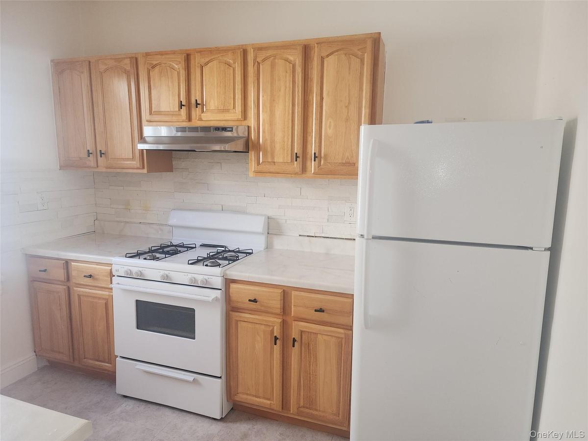 Kitchen featuring light wood cabinetry, white countertops, textured tile backsplash, a gas range, and a full-size refrigerator