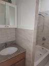 Bathroom featuring a white medicine cabinet, granite countertop vanity with wood-finish cabinetry, a white porcelain sink, and tiled bath surround wit