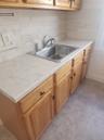Wood-finish cabinetry with black hardware, light-toned countertops, and a stainless steel sink