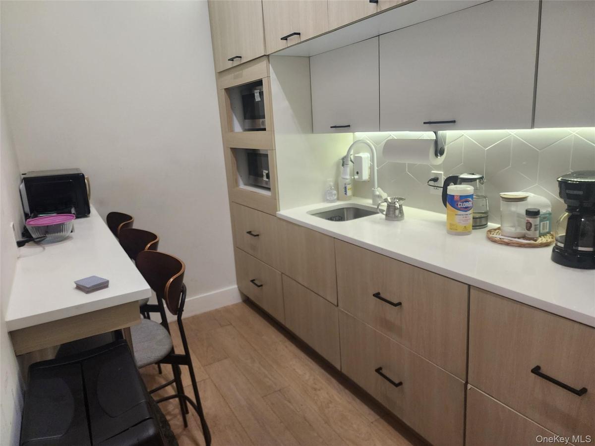Compact kitchen area featuring wood-finish flooring, light-toned cabinetry with dark hardware, built-in microwave, white solid surface countertops, an