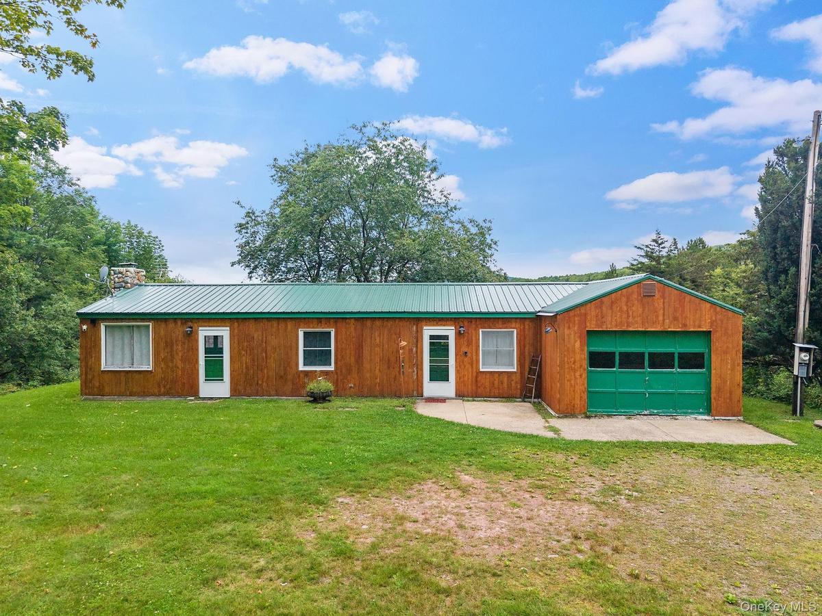 Wood-paneled exterior with a green metal roof, integrated garage featuring a green door, and multiple entry points