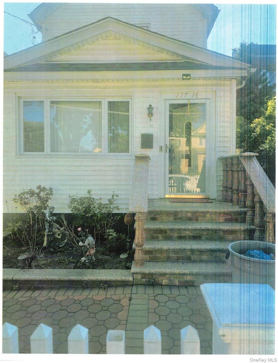 White picket fence, paver walkway, stone steps, front porch with decorative marble railing, and a windowed doorway.