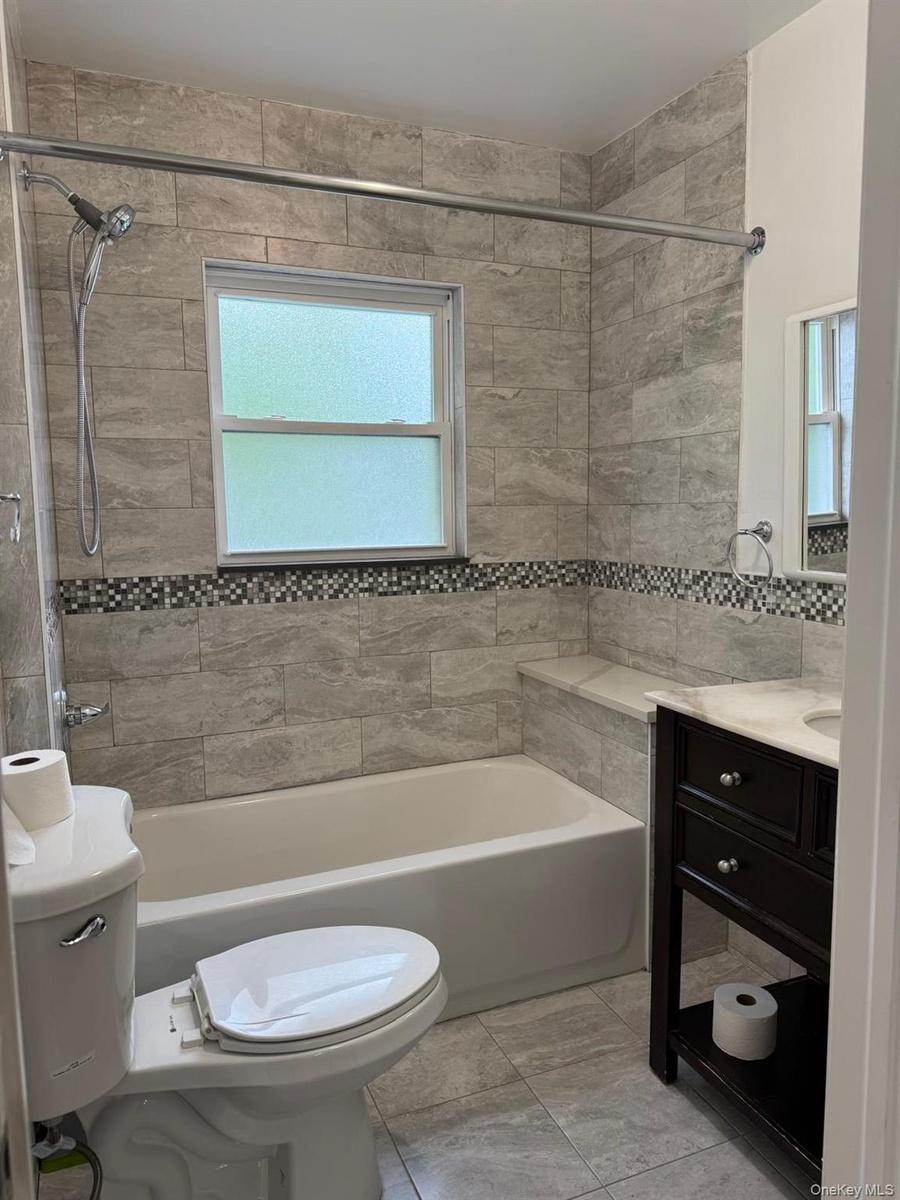 Bathroom featuring tiled walls, a built-in shower niche, a bathtub, and a dark wood-finish vanity with a white countertop