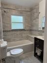 Bathroom featuring tiled walls, a built-in shower niche, a bathtub, and a dark wood-finish vanity with a white countertop