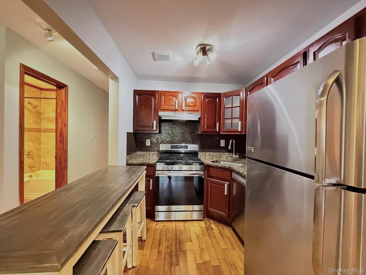 Kitchen featuring wood-finish flooring, stainless steel appliances, granite countertops, wood cabinetry, and a built-in breakfast bar