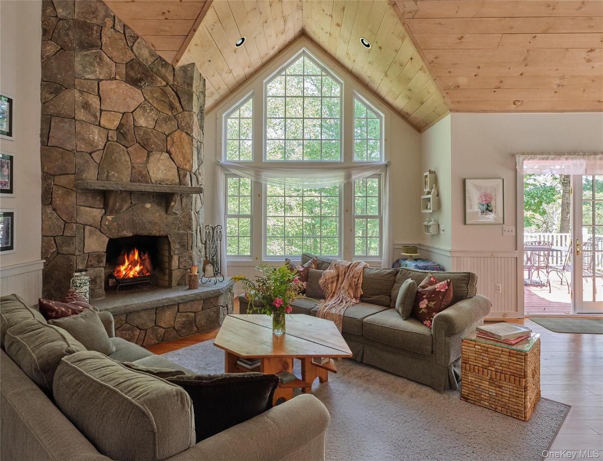 Living room with wainscoting, wood ceiling, a stone fireplace, high vaulted ceiling, and wood finished floors