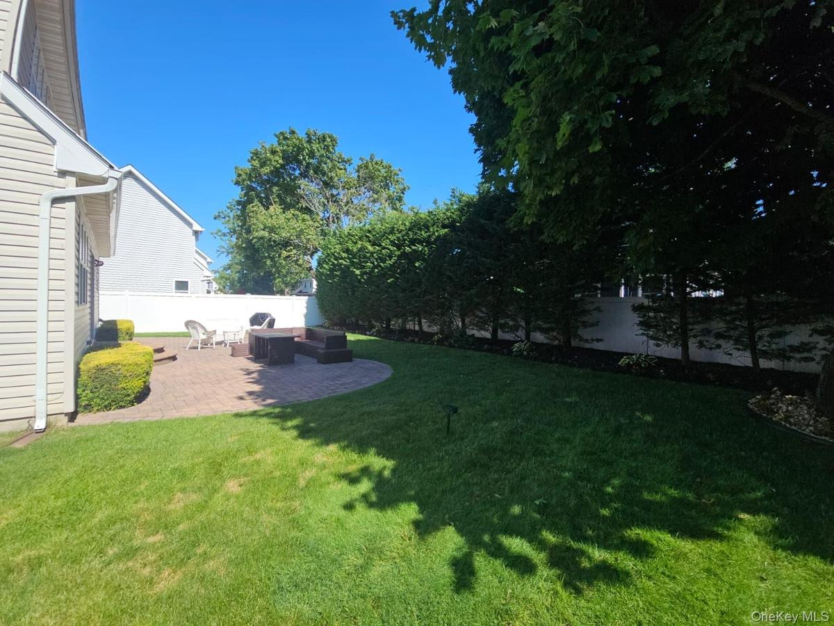 Expansive green lawn, paver patio, established privacy hedging, mature trees, and a white privacy fence